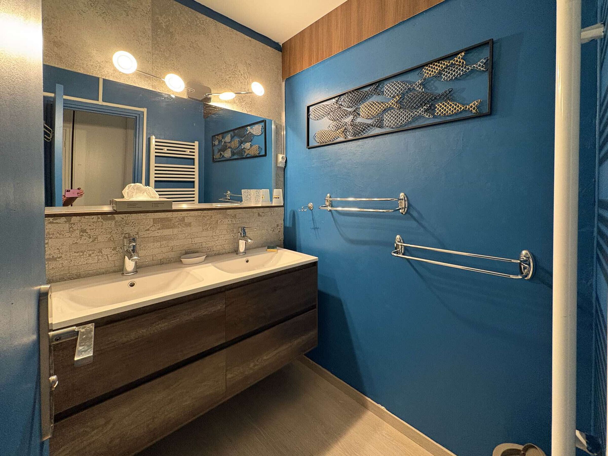 Une salle de bain avec un mur bleu, deux lavabos, un miroir et des porte-serviettes.
