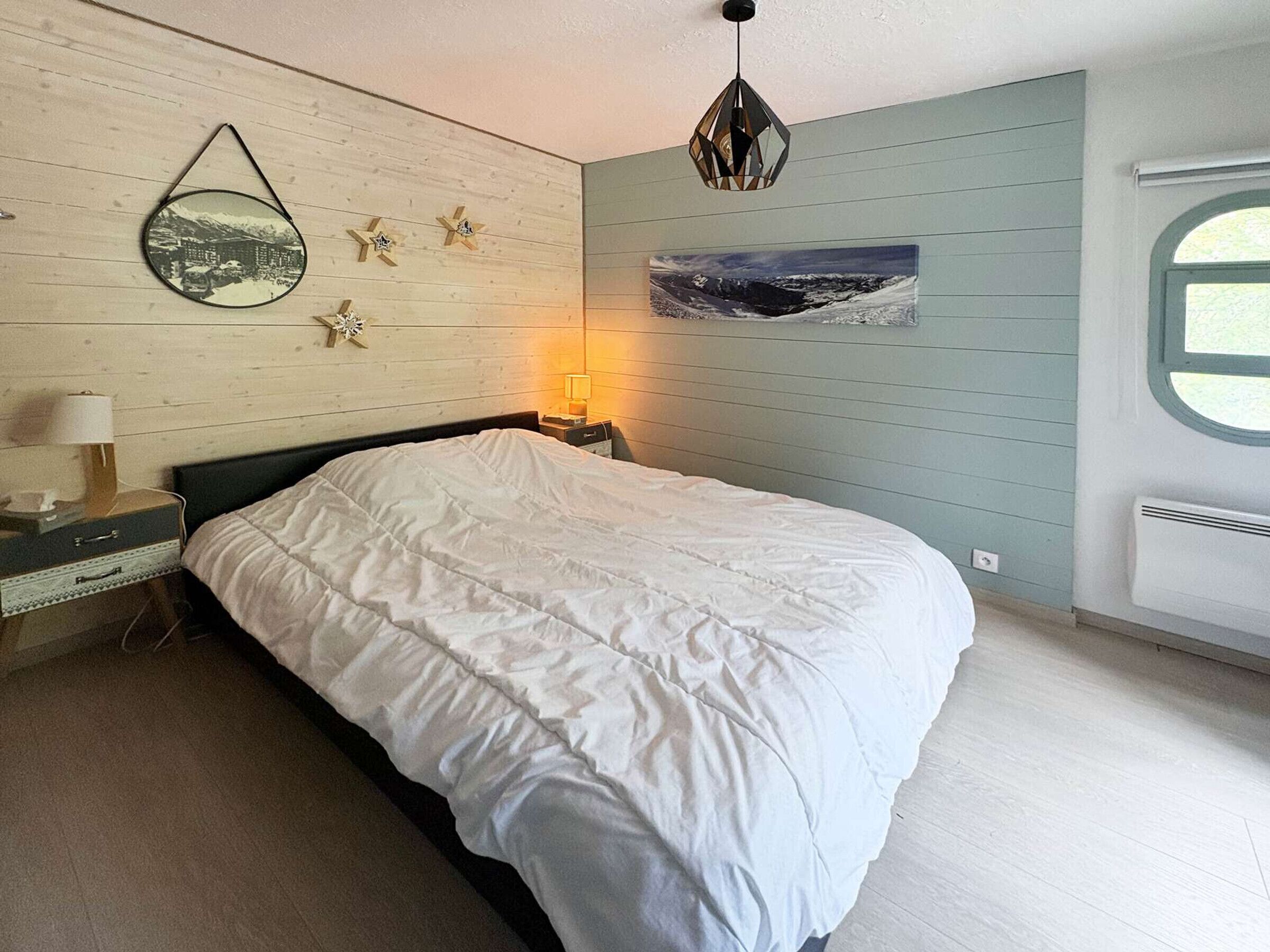 A bedroom with a bed, a nightstand, a lamp, a wall-mounted picture, and a window.