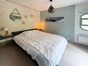 Ein Schlafzimmer mit Bett, Nachttisch, Lampe, Wandbild und Fenster.