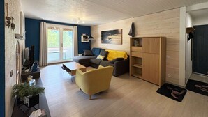 En moderne stue med en sofa, en gul farvet lænestol, et træskab og en skydedør til et udendørs område.