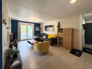 Ein modernes Wohnzimmer mit einer Couch, einem gelben Sessel, einem Holzschrank und einer Schiebetür zu einem Außenbereich.