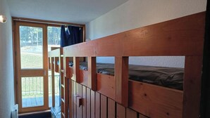 Un lit superposé avec une structure en bois, une fenêtre donnant sur un paysage verdoyant et une porte menant à l’extérieur.
