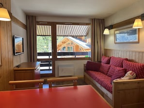 Ein gemütliches Zimmer mit einer Holzbank, einem roten Sofa, einem Fernseher und einem Fenster mit Blick auf eine Holzhütte.