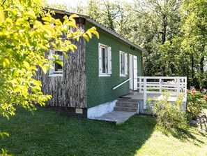 A small, single-story building with a green exterior, white trim, and a wooden deck with a white railing.