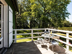 A wooden deck with a white railing, a table with two chairs, and a glass of wine.