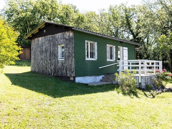 A small, single-story building with a green exterior and white trim. It features a front porch with a white railing and a small set of steps leading up to the entrance.