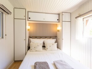 A bedroom with a bed, bedside lamps, a window, and a wooden ceiling.
