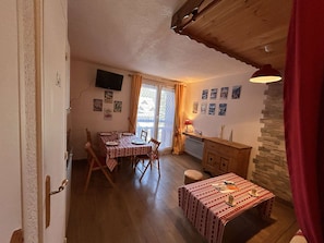 A cozy dining area with a table set for two, a small table with a single chair, a wooden cabinet, and a stone wall. - Apartment at the slopes - 6 guests (Risoul)