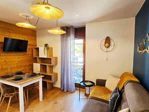 Ein Wohnzimmer mit Fernseher, Holzböden, einem Esstisch, einer Couch und einem großen Fenster.