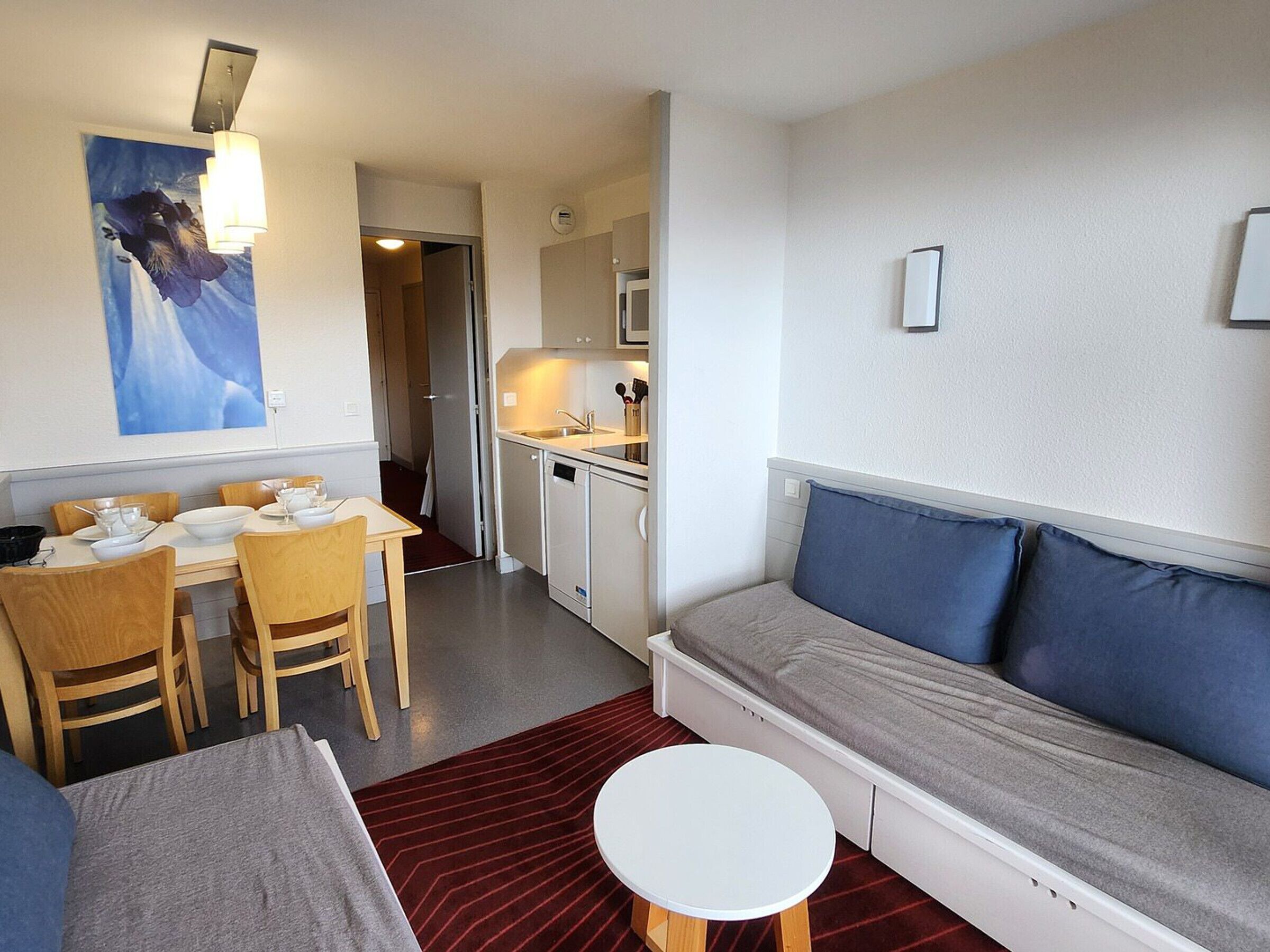 Kompakti hotellihuone, jossa on ruokailutila, pieni keittiö ja sohva koristetyynyineen.