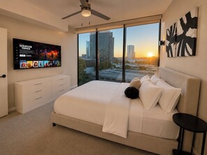 Een moderne slaapkamer met een groot bed, een aan de muur bevestigde televisie en uitzicht op de stad.