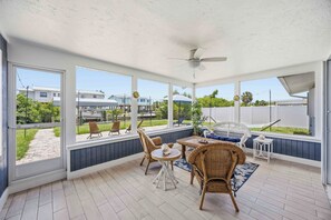Eine überdachte Terrasse mit Korbmöbeln, Deckenventilator und großen Fenstern.