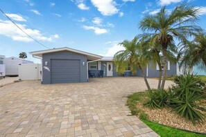 Ein Wohnhaus mit befestigter Auffahrt, Garage, einer Terrasse mit Gartenmöbeln und einer Palme.