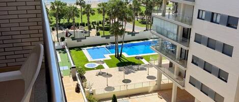 Vista de una piscina, palmeras y una playa desde un balcón.