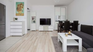 Una sala moderna con un televisor de pantalla plana, un sofá, una mesa de centro y un comedor con sillas.