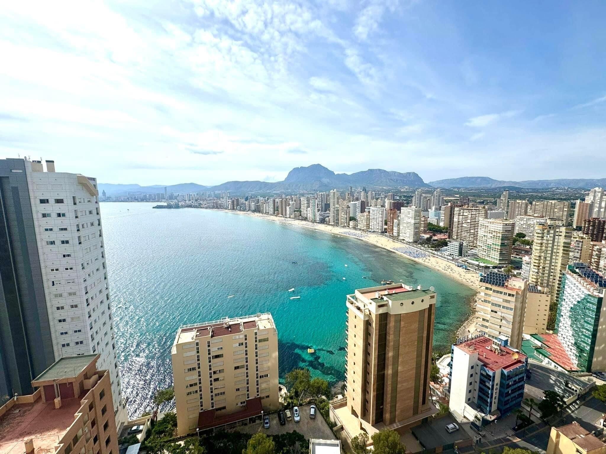 Eine Küstenstadt mit Hochhäusern, einem Strand und Bergen im Hintergrund.