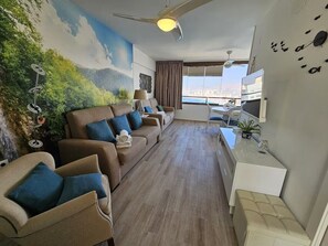 Ein modernes Wohnzimmer mit einer Sofagarnitur, einem Fernseher und einem Deckenventilator.