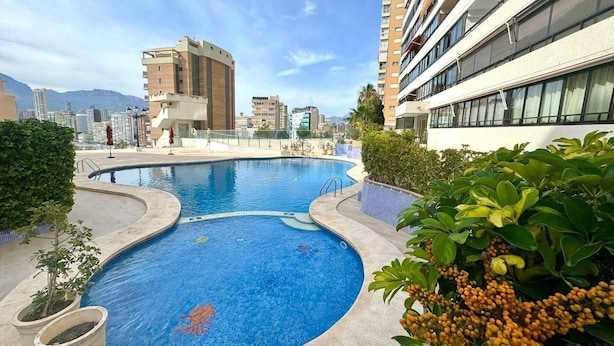 Una piscina en la azotea con vistas a un paisaje urbano, rodeada de vegetación y edificios modernos.