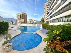 A rooftop swimming pool with a cityscape view, surrounded by greenery and modern buildings. - Panoramic Sunset Benidorm: Mediterranean Charm with Spectacular Views (Benidorm)