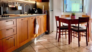 A kitchen with wooden cabinets, a stainless steel refrigerator, a dining table with chairs, and a window with a view of a building. - Stock 22:modern, central and close to the sea! Experience the city and the beach on foot (Trieste)