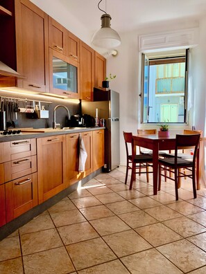 A kitchen with wooden cabinets, a stainless steel refrigerator, a dining table with chairs, and a window with a view of a building. - Stock 22:modern, central and close to the sea! Experience the city and the beach on foot (Trieste)