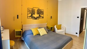 A bedroom with a large bed, a chair, a bedside table, and a wall-mounted artwork. - Stock 22:modern, central and close to the sea! Experience the city and the beach on foot (Trieste)
