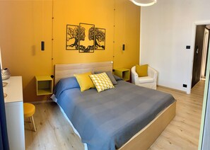 A bedroom with a large bed, a chair, a bedside table, and a wall-mounted artwork. - Stock 22:modern, central and close to the sea! Experience the city and the beach on foot (Trieste)
