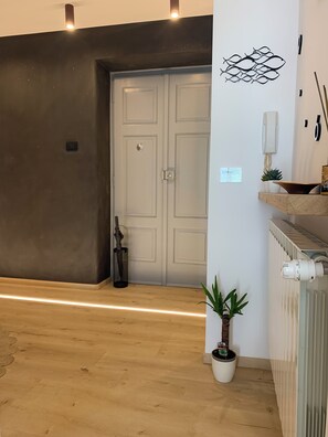 A hallway with a wooden floor, a white door, a potted plant, a wall-mounted light fixture, and a radiator. - Stock 22:modern, central and close to the sea! Experience the city and the beach on foot (Trieste)