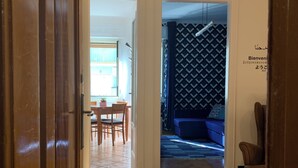 A hallway leading to a dining area with a table and chairs, a patterned wall, and a blue sofa. - Stock 22:modern, central and close to the sea! Experience the city and the beach on foot (Trieste)