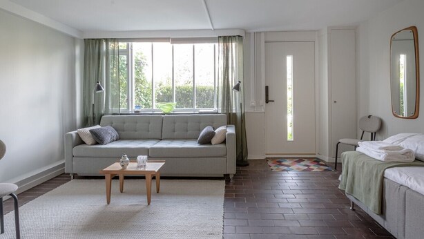 A room with a sofa, a small table, a bed, a mirror, and a door.