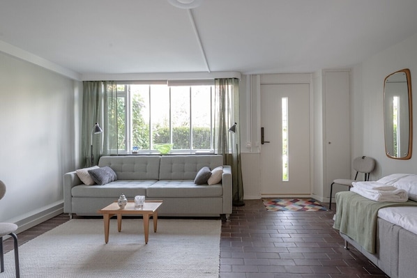 A room with a sofa, a small table, a bed, a mirror, and a door.