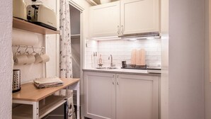 A compact kitchen with white cabinets, a stainless steel sink, and a drying rack.