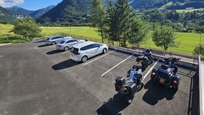 A parking area with cars and motorcycles, surrounded by green fields and mountains. - Le plein soleil (Vacheresse)