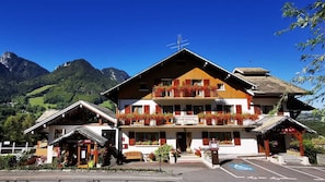 Un hotel con restaurante y bar, zona de estacionamiento y montañas al fondo.