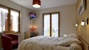 A bedroom with a bed, a red chair, a TV mounted on the wall, and a window with curtains. - Le plein soleil (Vacheresse)