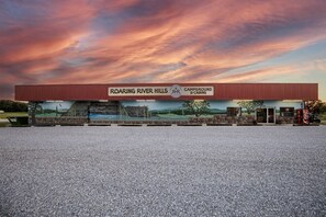 A campground and cabins building with a large sign, a gravel parking lot, and a mural depicting a river scene.