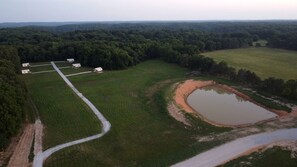 An aerial view of a rural property with a dirt road, a pond, and several small buildings.