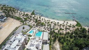 An aerial view of a resort with a beach, palm trees, and a swimming pool.