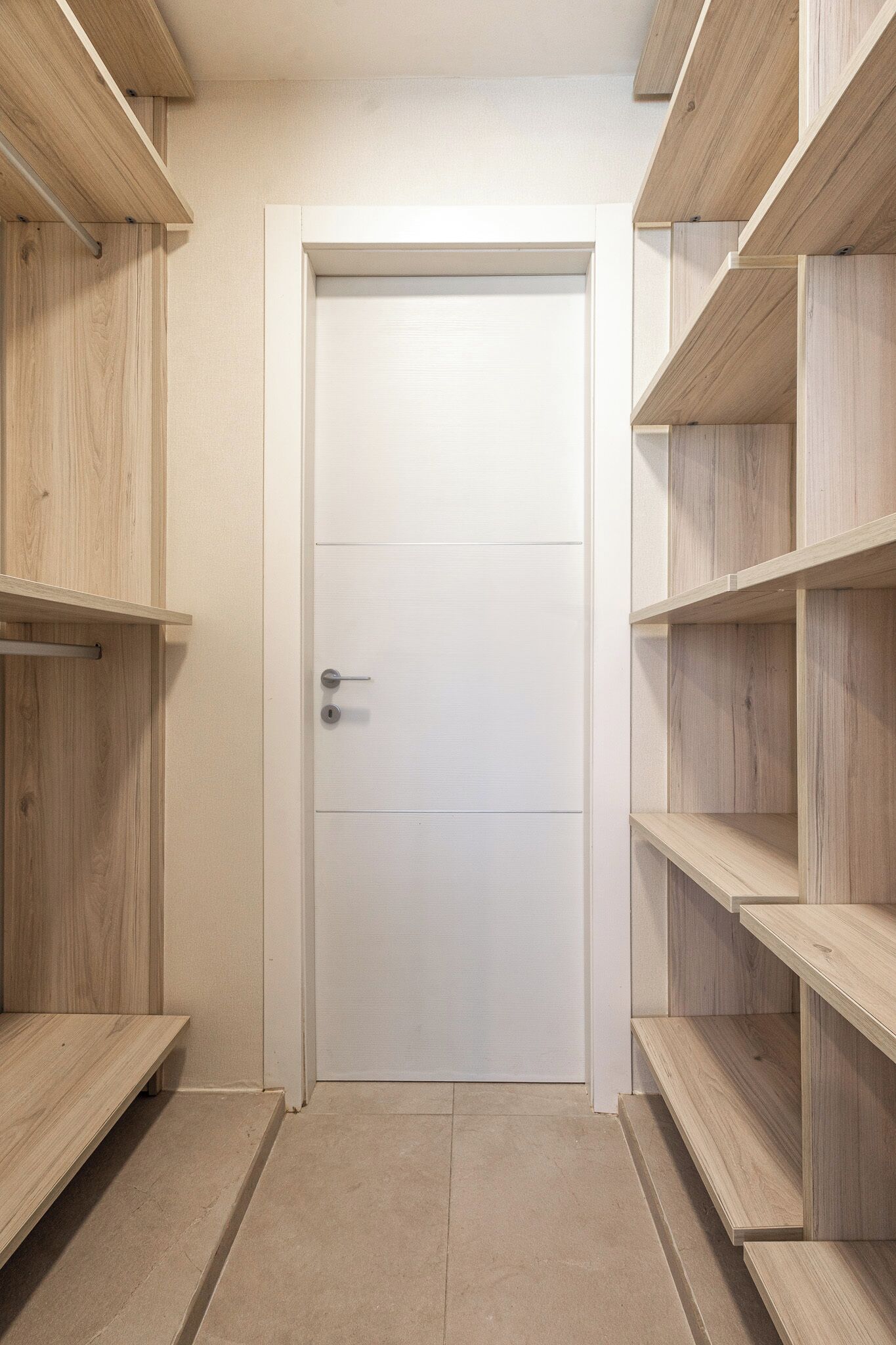 A hallway with a white door, wooden shelves, and a tiled floor.