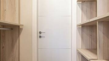 A hallway with a white door, wooden shelves, and a tiled floor.