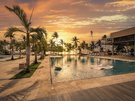 A swimming pool with palm trees, a lounge area, and a building with a modern design.. Luxury Beach Apt | Walk to Beach + Pool & Jacuzzi
