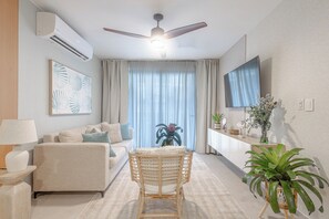 A modern living room with a sofa, a wicker chair, a flat-screen TV, and a ceiling fan.