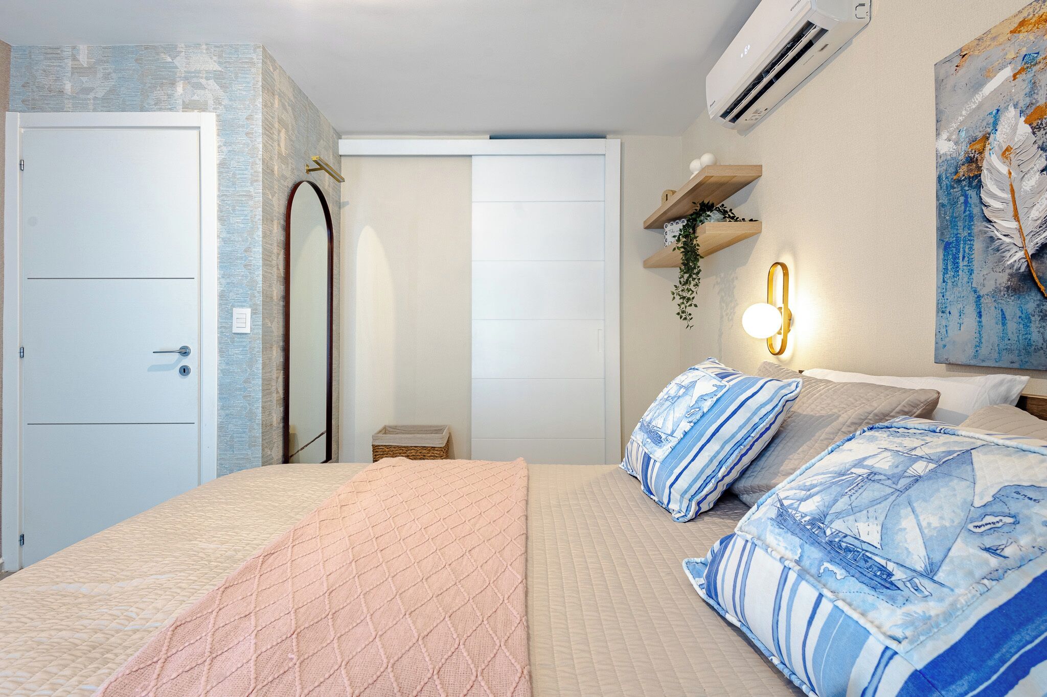 A bedroom with a bed, a wardrobe, a mirror, a wall-mounted air conditioner, and a shelf with a plant.
