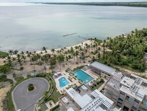 An aerial view of a resort with a swimming pool, beach, and palm trees.