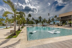 A swimming pool with lounge chairs, palm trees, and a building in the background.