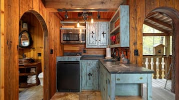A rustic kitchen with wooden walls, a central island, and a view of the outdoors.