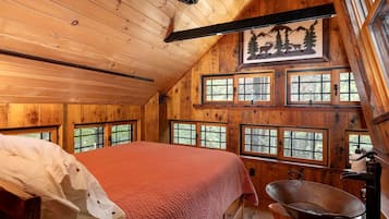 A cabin with a bed, multiple windows, a wooden ceiling, and a rustic decor.