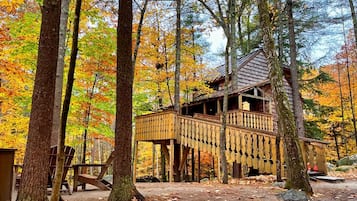 A wooden cabin with a deck, surrounded by trees with autumn foliage.