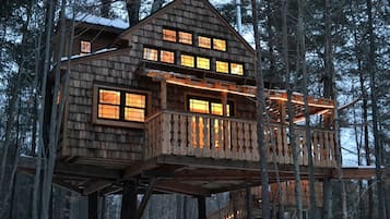 Une cabane en bois dotée de nombreuses fenêtres et d’un balcon, entourée d’arbres et de neige.