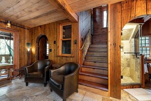 Un intérieur en bois avec un escalier, des fauteuils en cuir et un sol en pierre.
